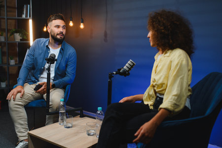 Two content creators, a man and a woman, are recording a podcast in a professional studio, engaging in conversationの写真素材