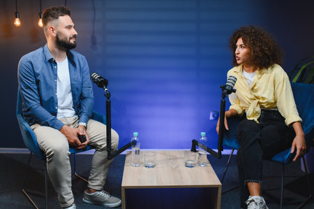 Two podcasters are recording a show in a professional studio, engaging in conversation and sharing...
