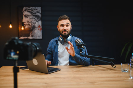 Young man recording a video blog using professional equipment in his home studio, gesturing while speakingの写真素材