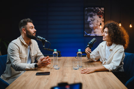 Two podcasters, a man and a woman, are recording audio content in a professional studio, engaging in...