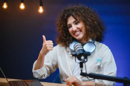 Young woman giving thumbs up gesture while recording a video blog in a professional studio, using a...