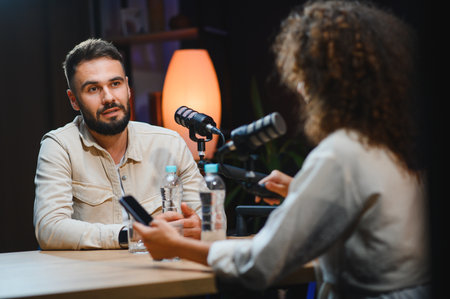Two content creators, a man and a woman, recording a podcast in a professional studio, using...