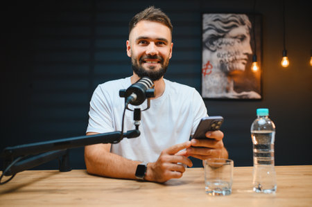 Young man recording audio content using professional microphone and smartphone in his home studioの写真素材