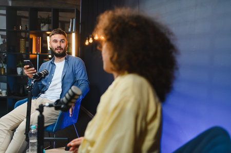 Two content creators recording a podcast using professional microphones and a smartphone in a modern...