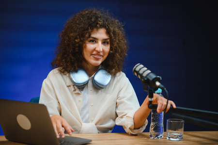 Female podcaster creating audio content, using laptop and professional microphone in modern studio...