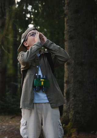 Young boy scout wearing binoculars and a backpack, shouting for help while navigating through a...