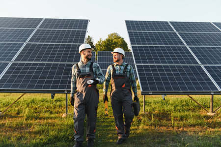 Engineers walking through a solar power plant, holding blueprints and tools, collaborating on...
