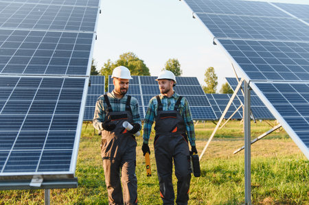 Two engineers with hard hats and overalls walking through a solar farm, discussing plans for...