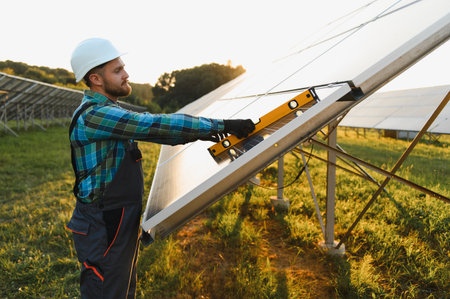 Worker in safety helmet and uniform checking alignment of a solar panel, ensuring efficient...