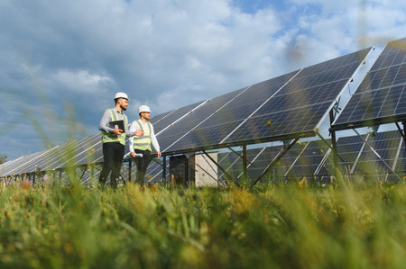 Engineers in safety vests and helmets examining solar power panels in a field, symbolizing renewable energy and sustainabilityの写真素材