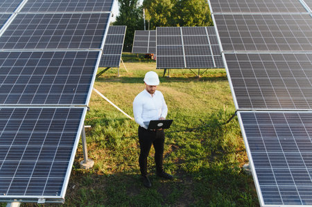Man in a hard hat using a laptop, checking solar panels. Focusing on clean, sustainable energy...