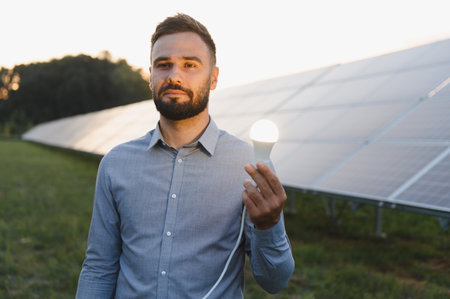 Man presenting an illuminated led light bulb against a backdrop of photovoltaic solar panels,...
