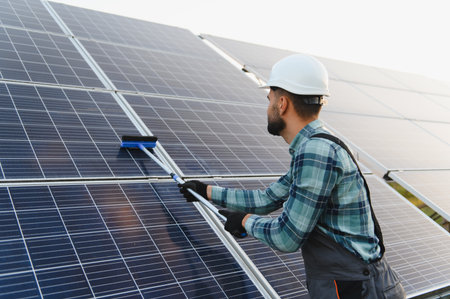 Worker in hard hat cleaning solar panels with a brush, ensuring efficient green energy production...