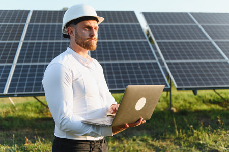 Engineer in hard hat and white shirt using laptop to monitor solar panels and analyze renewable...