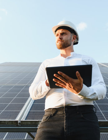 Engineer wearing hard hat checking solar panel performance on a photovoltaic power station using a...