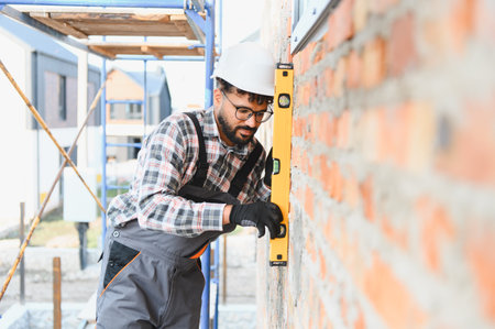 Construction worker in hard hat and safety glasses checking the level of a newly built brick wall at...