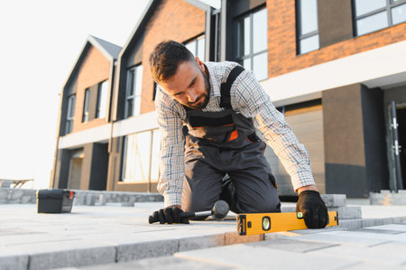 Construction worker carefully laying pavement blocks, using a spirit level to ensure a perfectly...