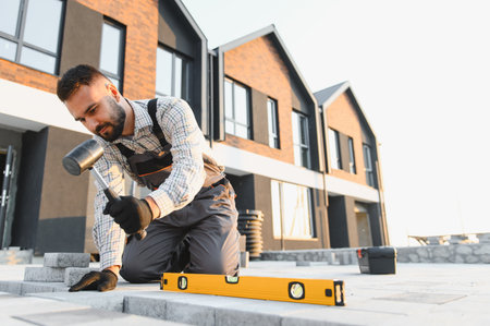 Young man installing paving stones for a new walkway at a modern housing construction site,...