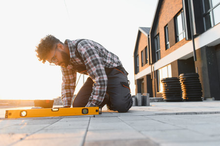 Worker installing paving stones at a residential construction site, using a spirit level to ensure a precise, even pathway surfaceの写真素材
