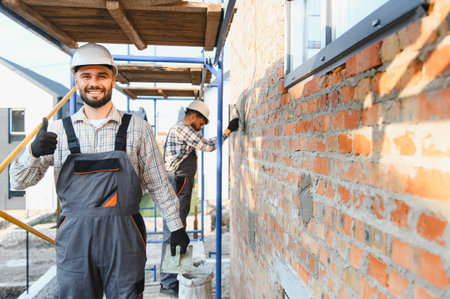 Team of happy construction workers building a brick wall on scaffolding, showing teamwork and...