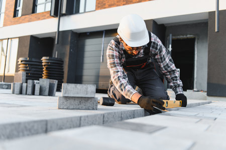 Worker carefully leveling concrete pavers, improving the exterior of a modern building with precise...