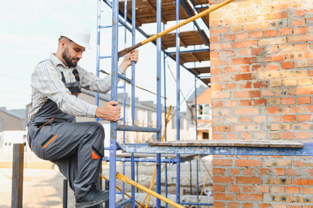 Construction worker wearing hard hat and uniform climbing metal scaffolding, working on residential...
