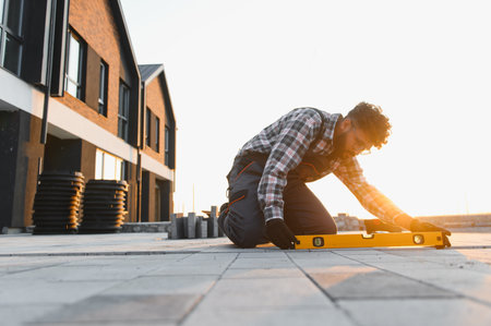 Construction worker kneeling, checking the level of newly laid paving on a modern building site at sunsetの写真素材