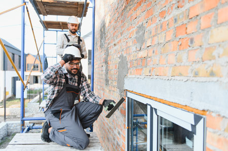 Construction workers applying plaster to a brick wall on scaffolding, building a new house....