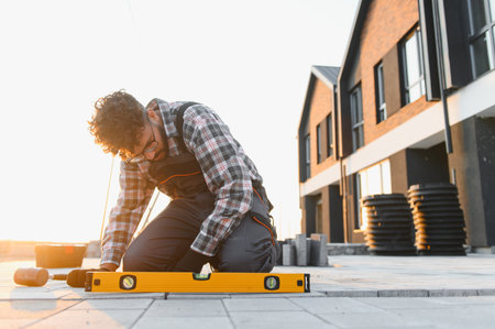 Worker checking the level of paving stones on a construction site, ensuring precise outdoor surface...
