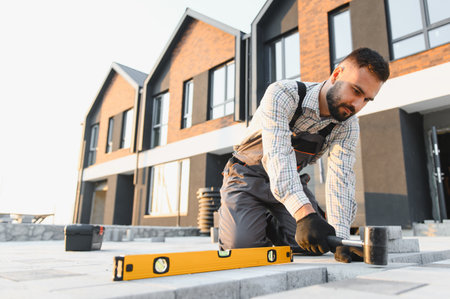 Professional construction worker installing concrete paving slabs for a modern house sidewalk, using...
