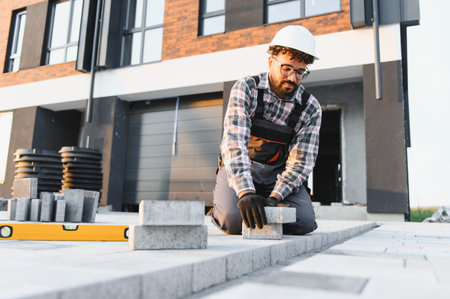 Skilled construction worker installing new paving on sidewalk in front of residential house, ensuring precise hardscapeの写真素材