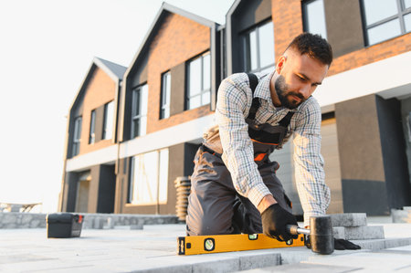 Construction worker carefully laying outdoor paving stones using a level and rubber hammer around a new buildingの写真素材