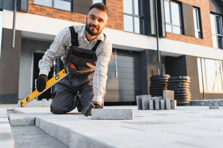 Male worker installing paving stones and checking alignment with a spirit level, building a new...
