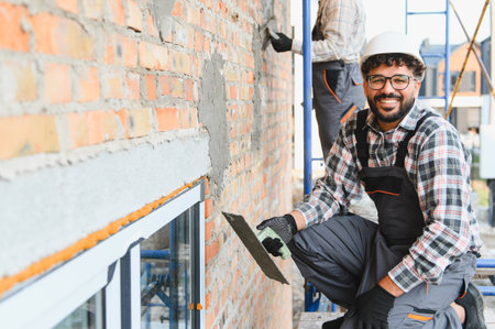Happy construction worker using a trowel to apply plaster to a brick wall, building a house on scaffoldingの写真素材