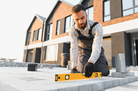 Professional worker installing new pavement, ensuring a perfect surface using a spirit level at a...