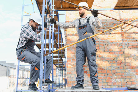 Two skilled construction workers assembling scaffolding, demonstrating teamwork and professional construction safety practices at a building siteの写真素材
