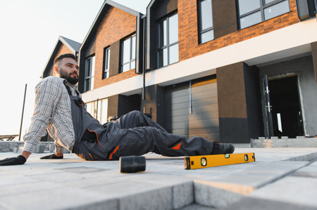Male builder in uniform resting on new interlocking pavers, taking a break from hard work outside...