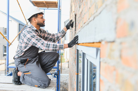 Construction worker in hard hat and protective gear applying plaster on new brick wall during house...