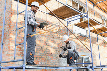 Team of construction workers on scaffolding applying plaster to a brick wall. People renovating a...