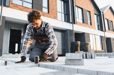 Man in workwear installing paving stones for a new patio floor. Construction and hardscape work on...