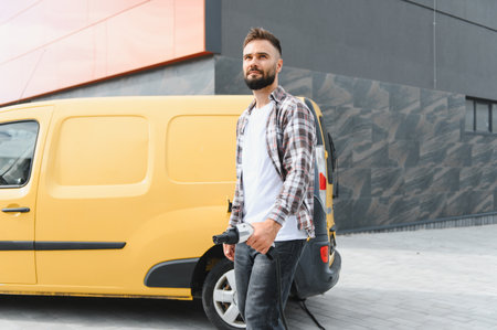 Delivery driver holding charging cable near his electric van parked near charging station in the...