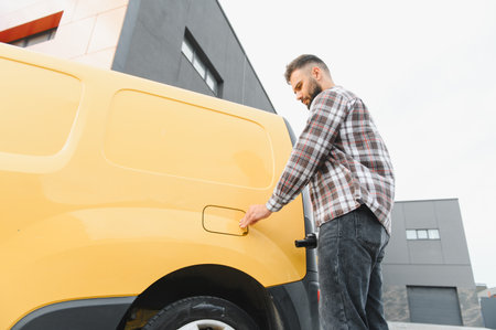 Delivery driver opening the fuel tank cap of a bright yellow van, getting ready for an important...