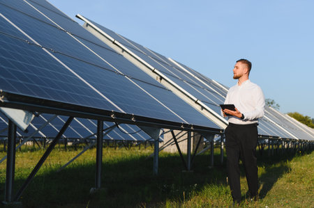 Young man using a digital tablet while inspecting a large solar panel array, focusing on renewable...