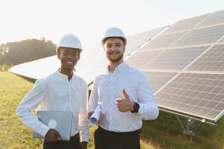 Two diverse engineers smiling, standing in a solar panel field at sunset, representing teamwork in...
