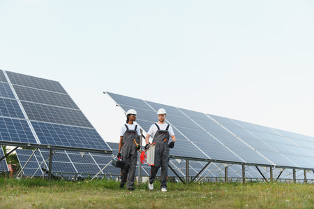 Engineers in protective workwear carrying tools, walking through a solar panel array establishing...