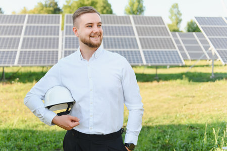 Young man working in renewable energy, standing outdoors with solar panels, thinking about...