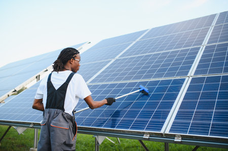 Technician cleaning solar panels at a power station, performing maintenance for sustainable green...