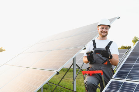 Solar technician performing installation work at a solar power plant, holding a drill and giving a...