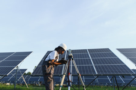 Black woman engineer using a surveying instrument at a solar power plant, working with renewable energy technologyの写真素材