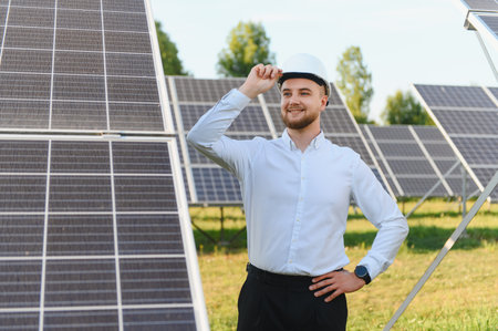Young engineer man wearing a hard hat, standing on a solar farm, working with renewable clean energy...